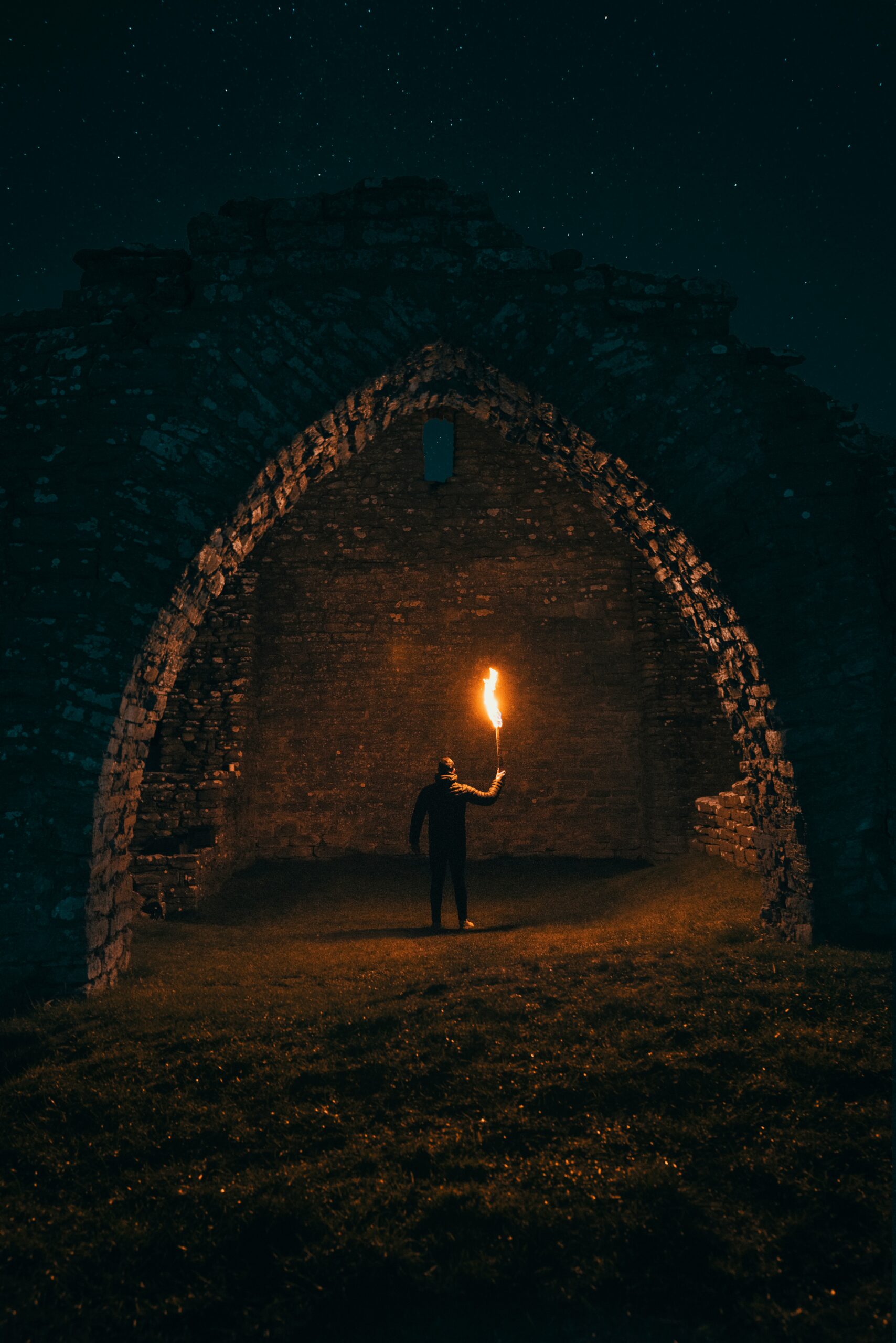 dark castle tunnel. Below the arch there's a man holding a torch.