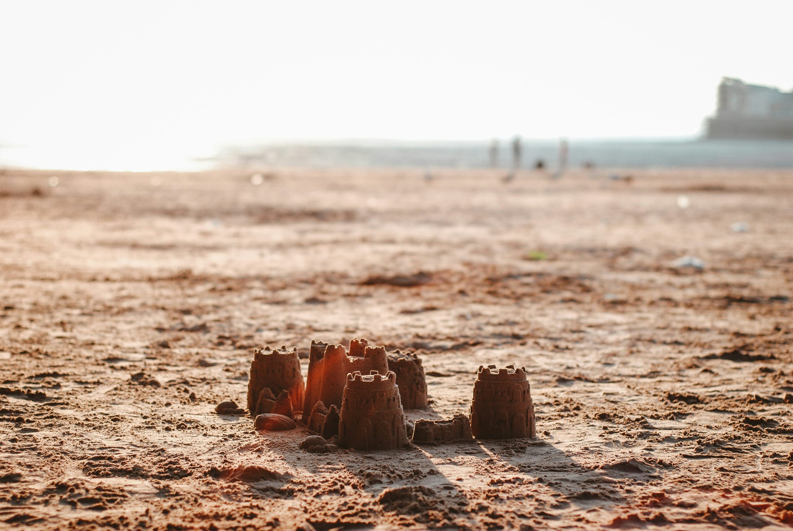 A sandcastle on a beach. Light is streaming between the towers.