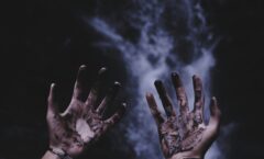 Two hands in front of an ocean, covered with mud or blood.