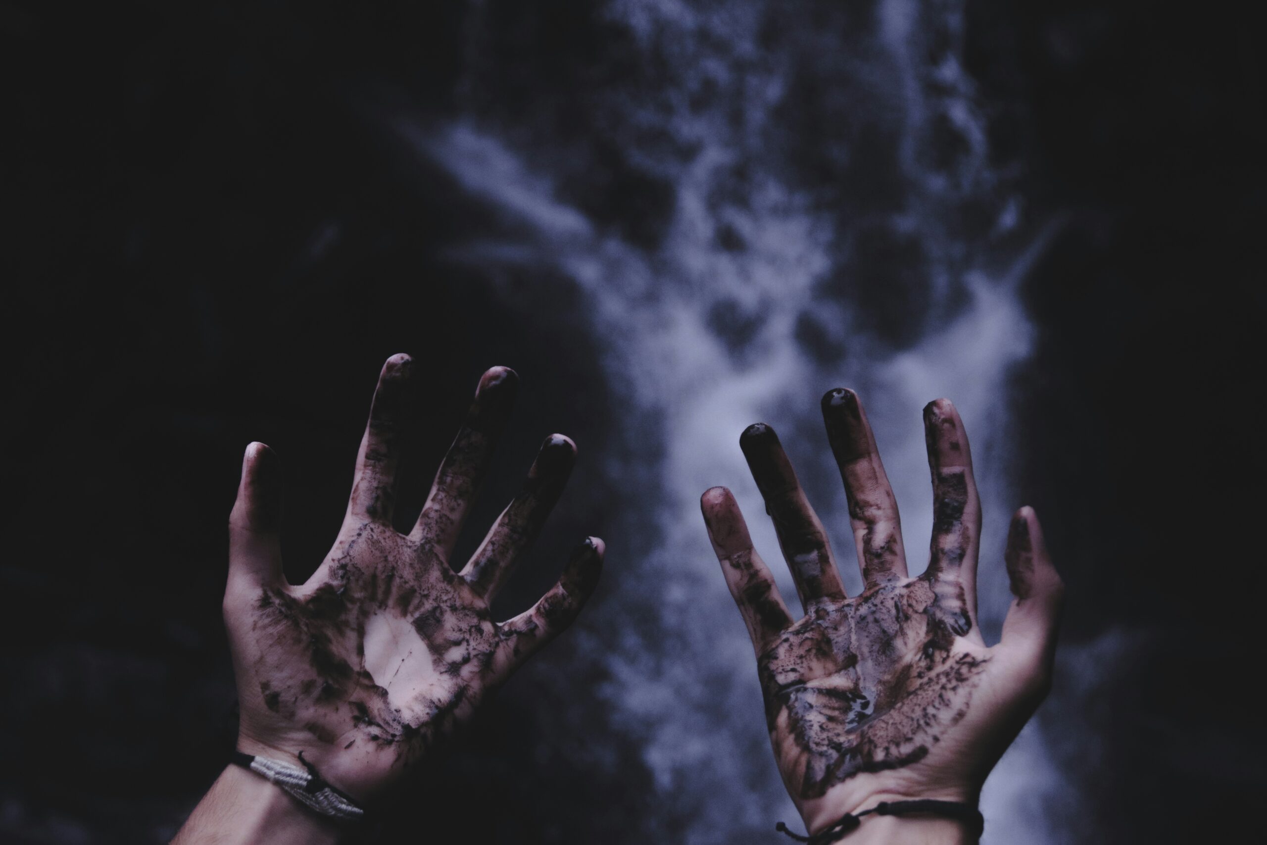 Two hands in front of an ocean, covered with mud or blood.